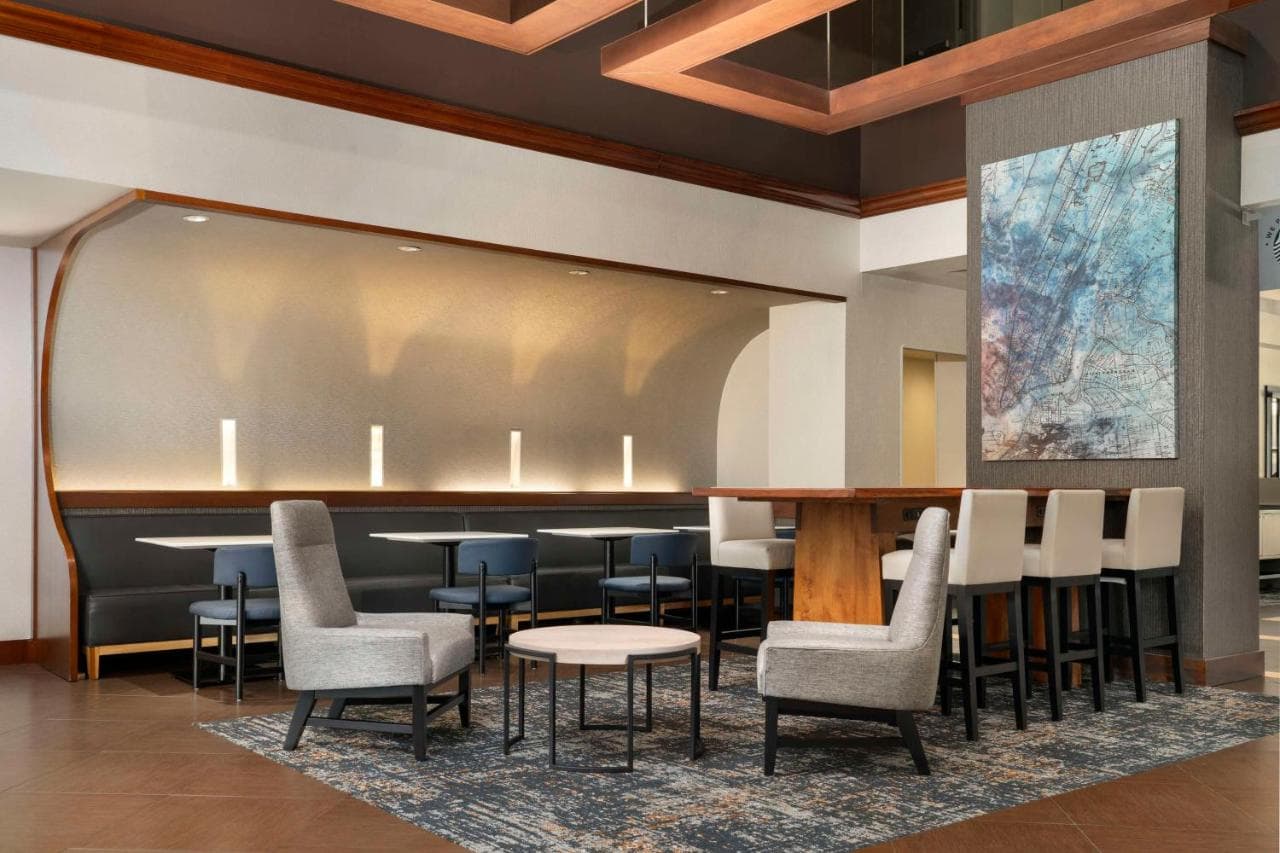 A modern seating area at Hyatt Place Secaucus, featuring a mix of cozy lounge chairs, high-top bar stools, and booth seating with ambient lighting.