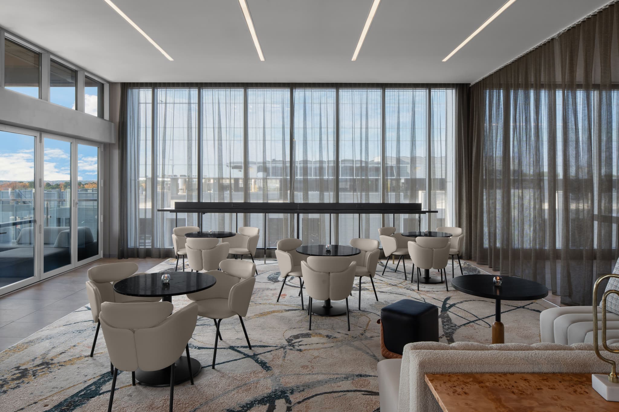 A stylish lounge area at AC Hotels Raleigh Level 7, with lounge seats and tables, with full height window