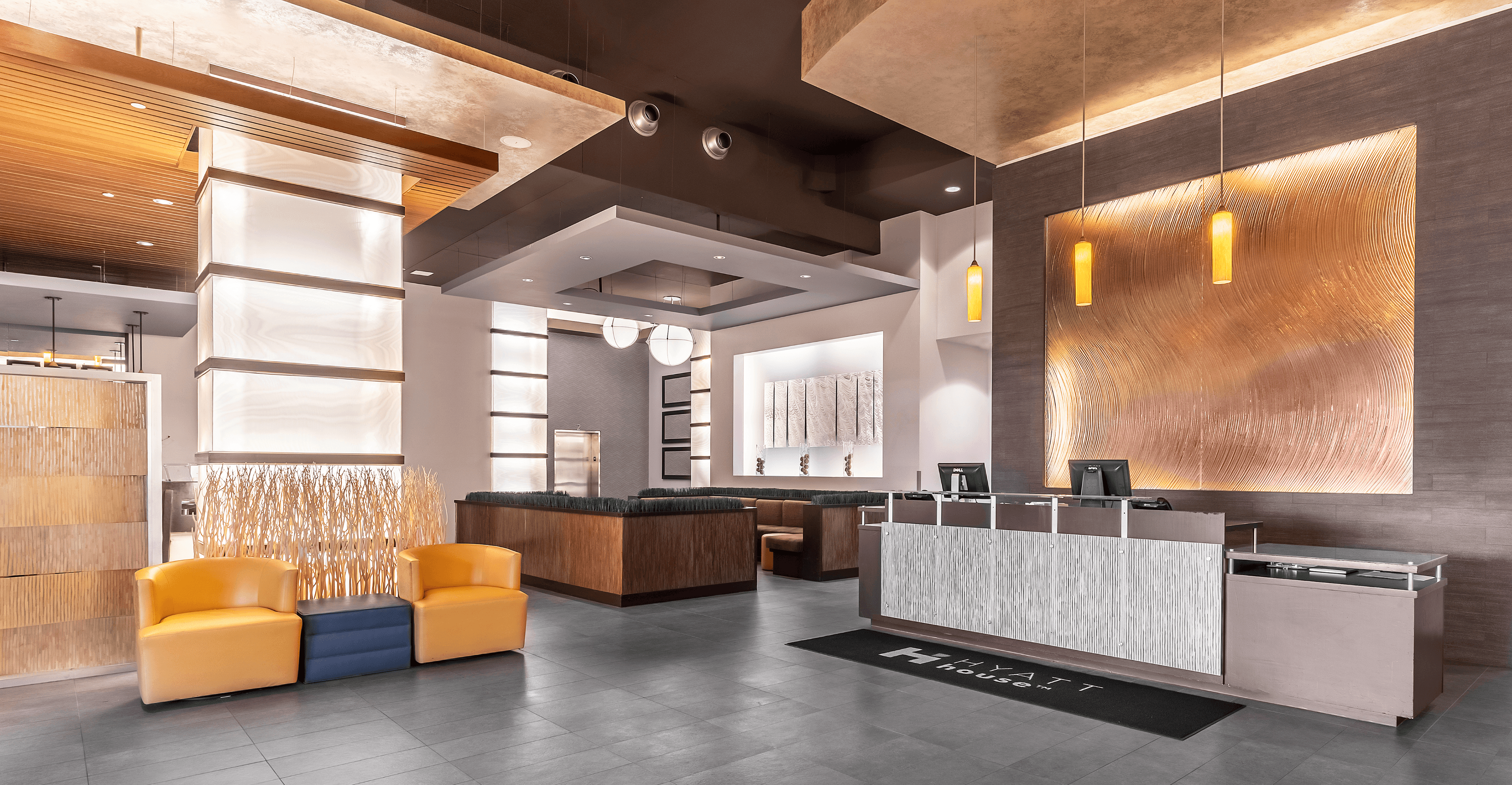 The front desk at Hyatt House Richmond Short Pump, featuring a modern and stylish reception area with warm lighting, textured wall accents, and sleek furnishings.